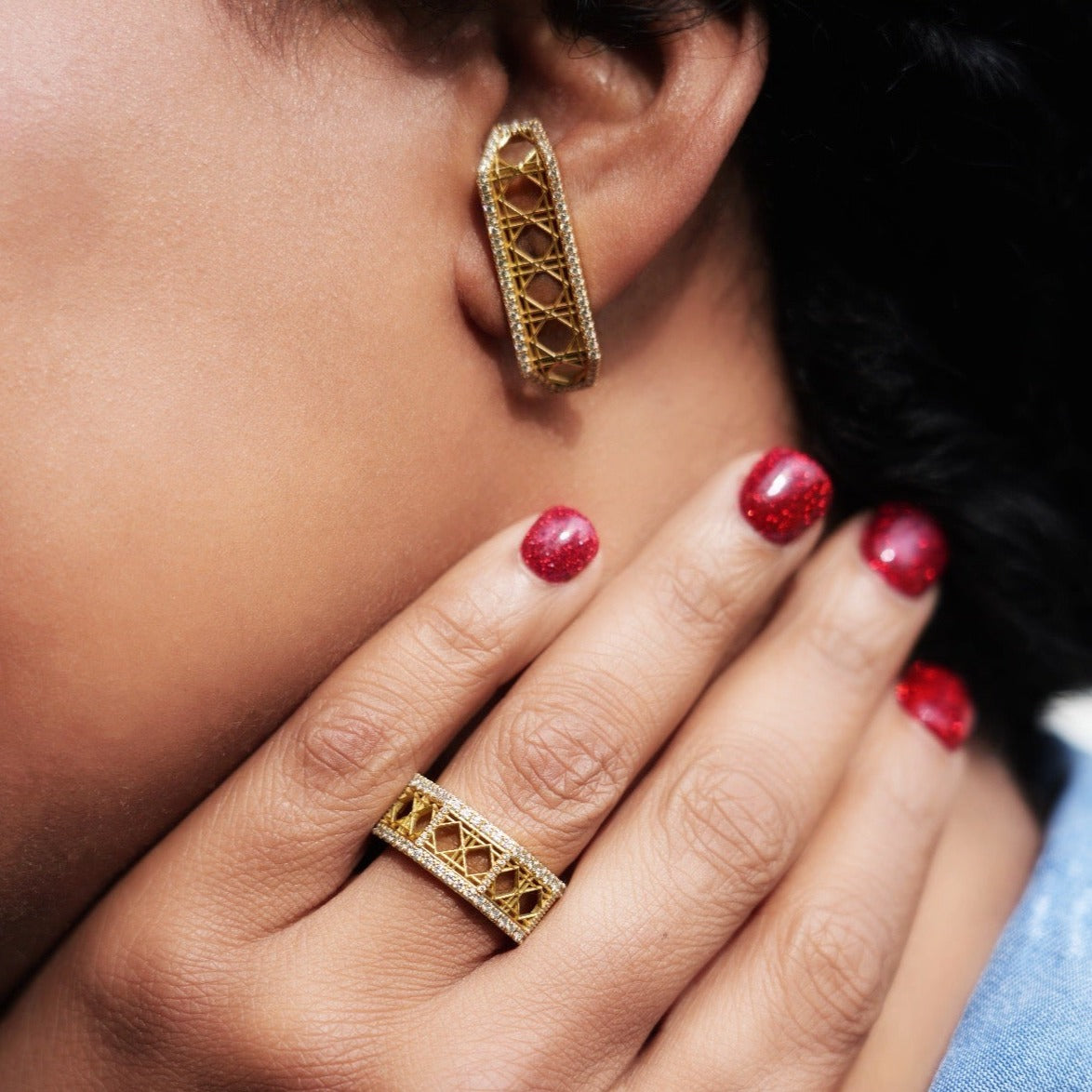 Model wearing MoAnA LUU Doudou cuff earrings and rings in 18K yellow gold, featuring geometric woven openwork design inspired by Caribbean fish traps.