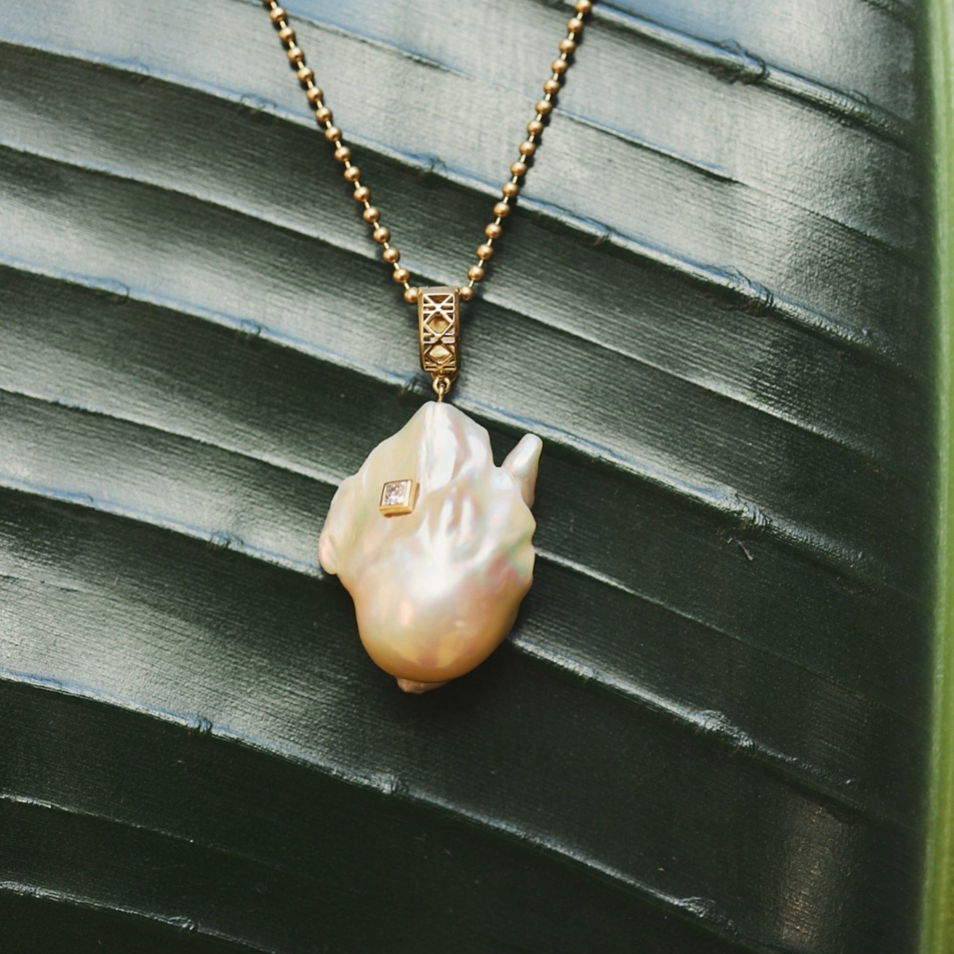 MoAnA LUU Abyss South Sea baroque pearl amulet in 18K yellow gold, featuring an oversized golden pearl pendant with diamond detail and signature cane-woven bail inspired by Caribbean fish traps.