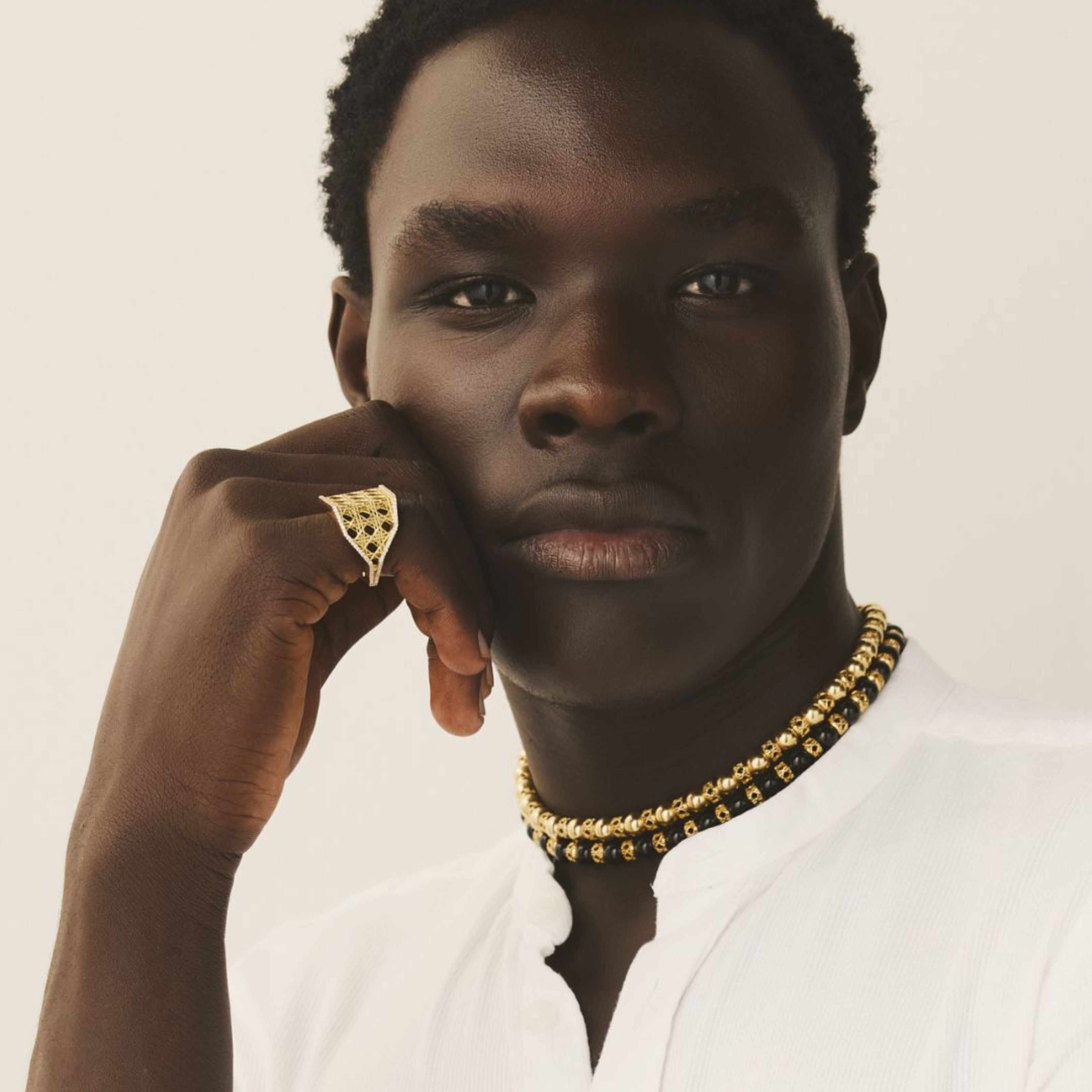 MoAnA LUU 18K yellow gold fine jewelry layered on male model, featuring Yva beads in 18K gold and onyx and a sculptural gold ring inspired by Creole design.