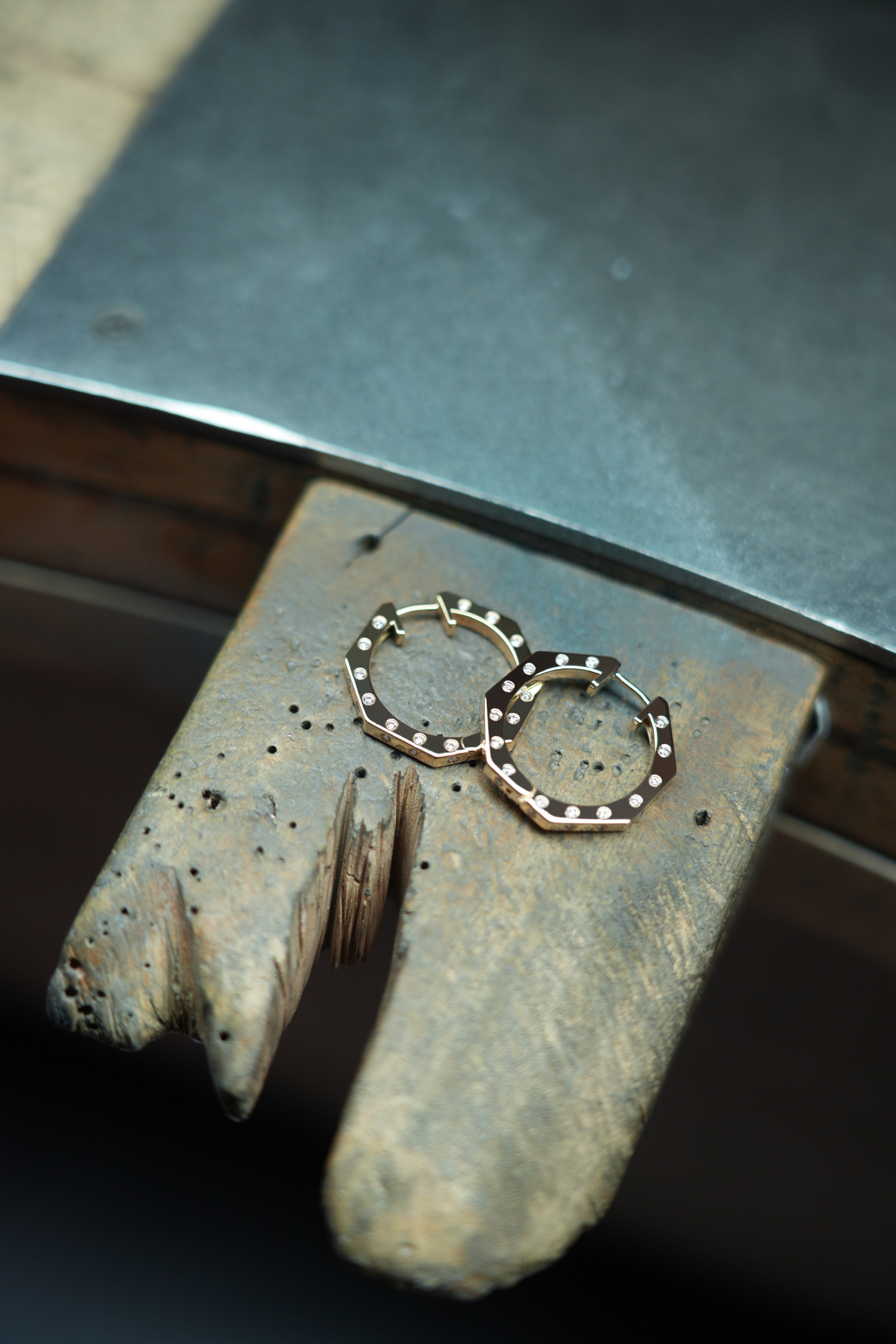 MoAnA LUU Ti hoop earrings in gold with diamond accents, featuring angular geometric design, displayed on a jeweler’s workbench.