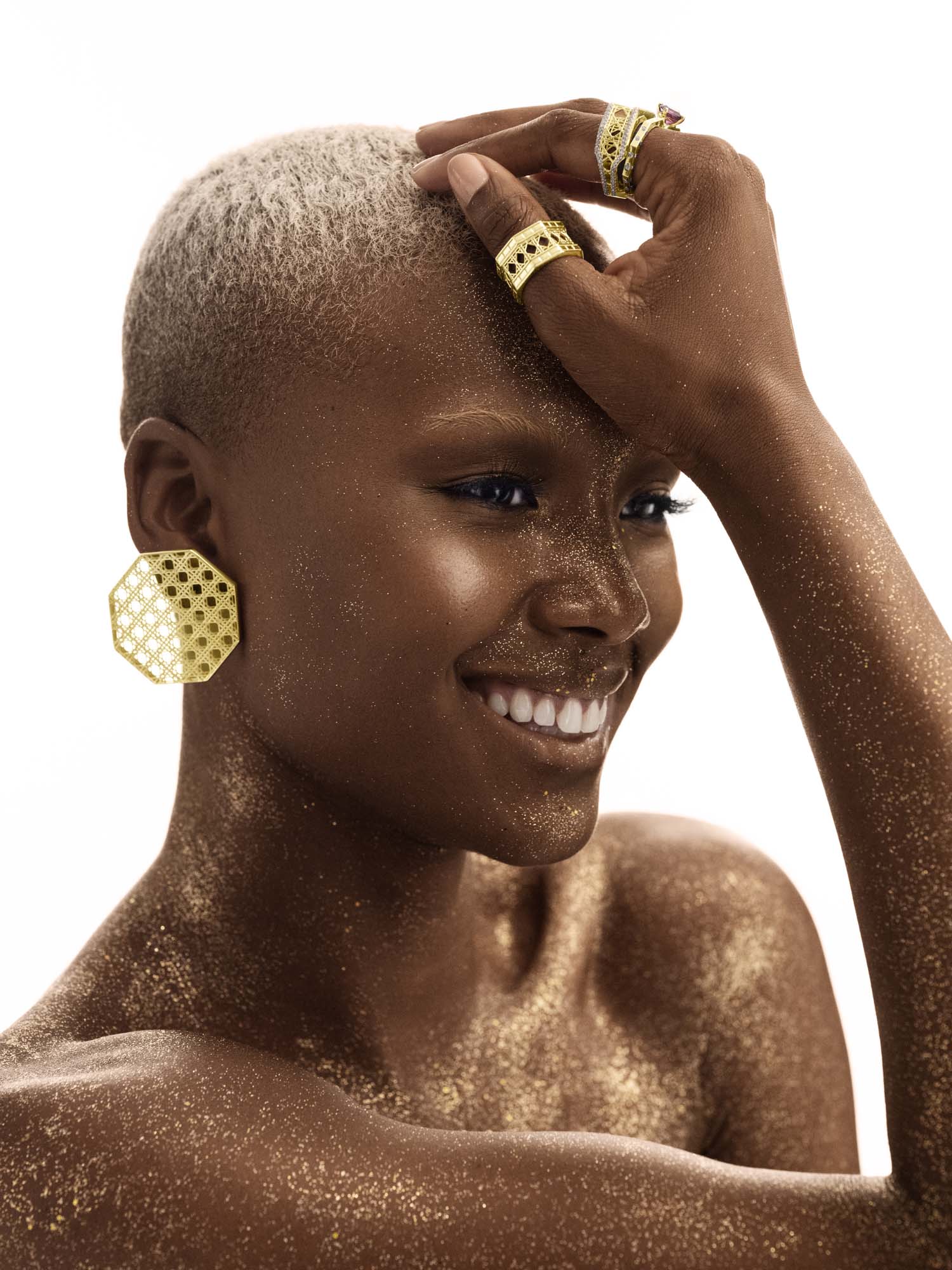 Model wearing MoAnA LUU Doudou statement octogonal earrings and rings in 18K yellow gold, featuring geometric woven openwork design inspired by Caribbean fish traps.