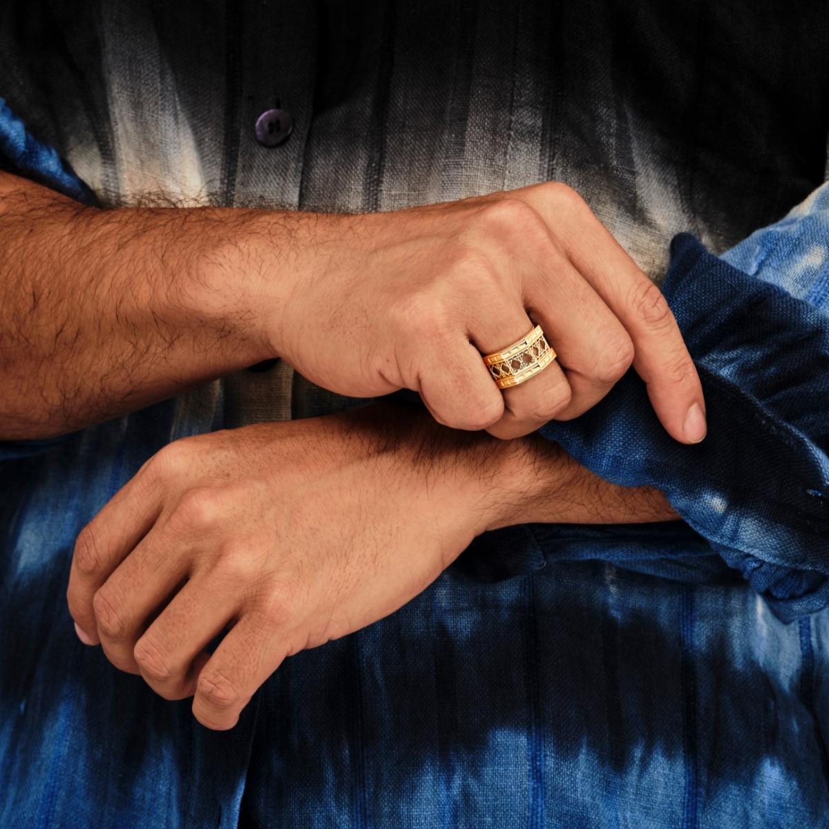 MoAnA LUU Doudou wide band ring in 18K yellow gold, worn on a male model’s hand, featuring an intricate geometric openwork cane design inspired by Caribbean fish traps.