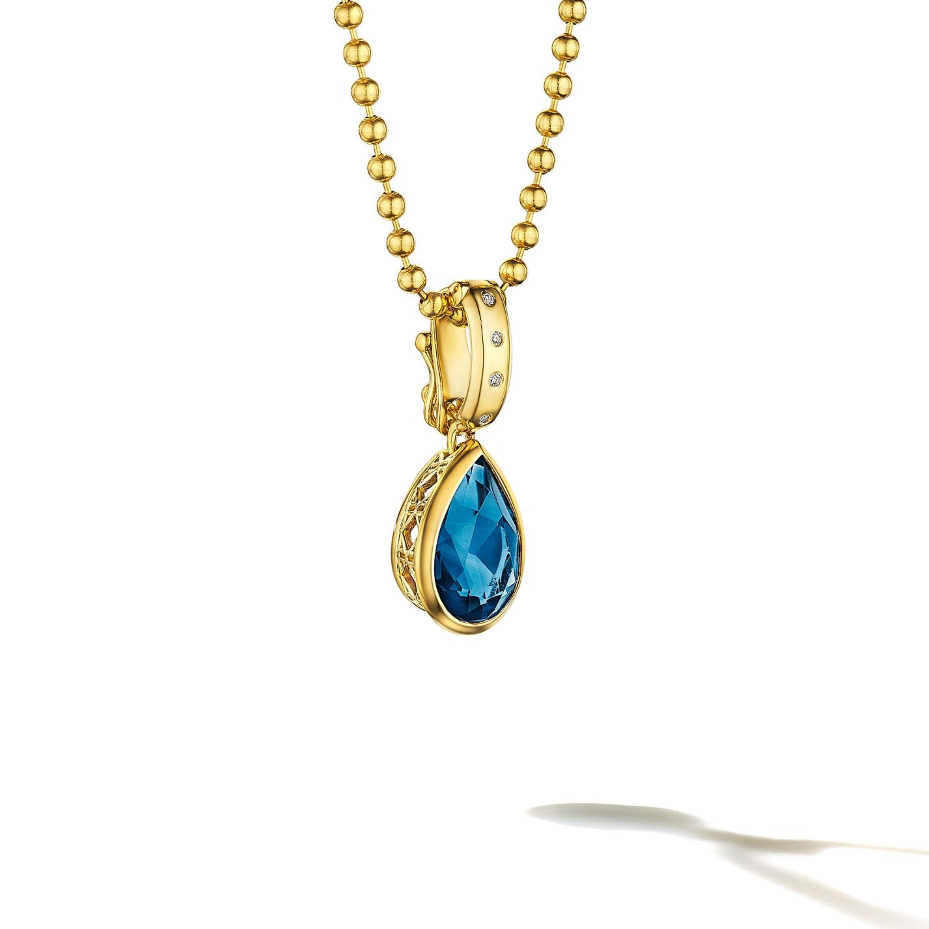MoAnA LUU Dlo pear-shaped London blue topaz pendant in 18K yellow gold, featuring a cane-woven frame inspired by traditional Caribbean fish traps, reflecting the house’s vision of Creole-inspired fine jewelry crafted in New York