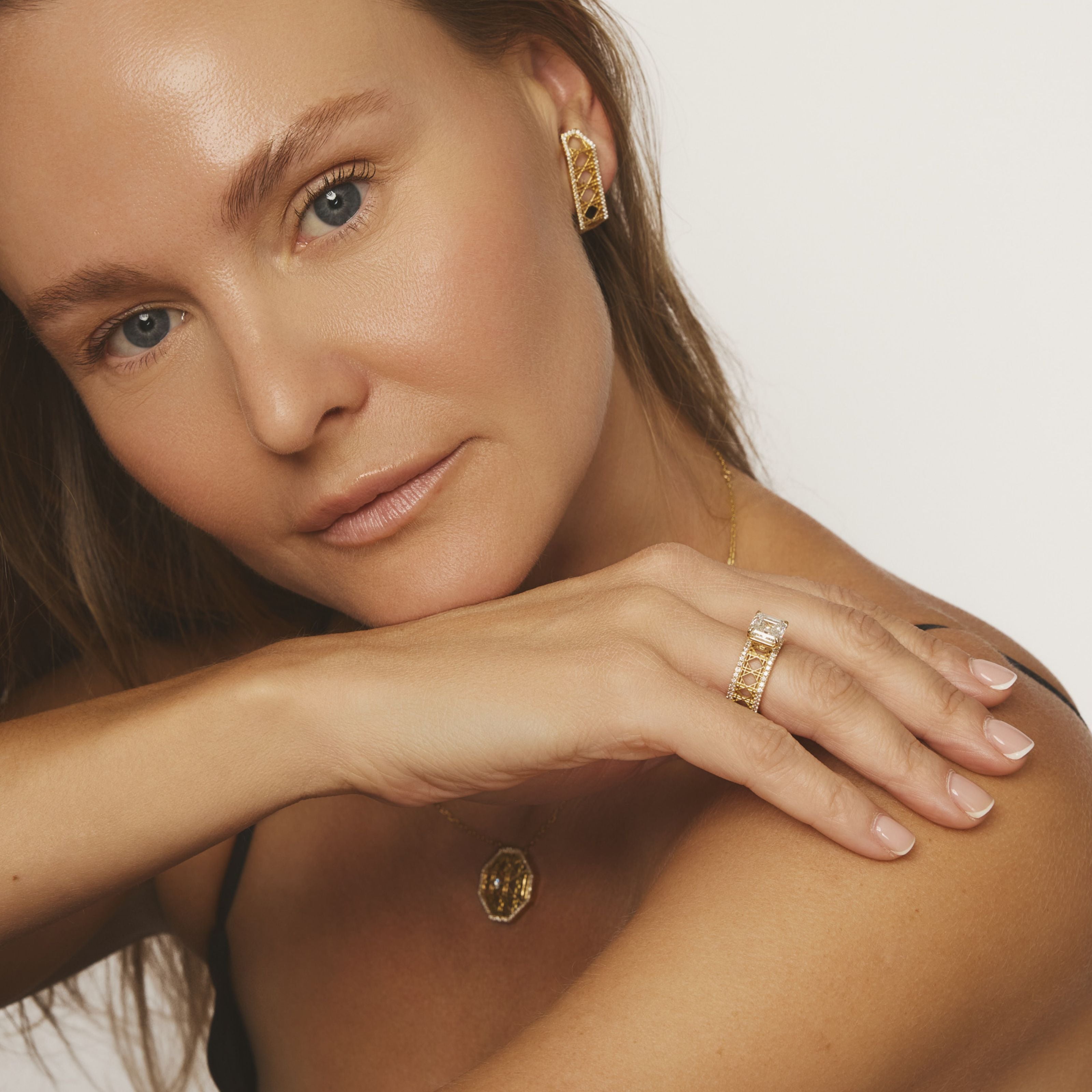 Model wearing MoAnA LUU Doudou earrings, pendant and engagement ring in 18K yellow gold, pavé diamonds and cushion cut solitaire, featuring cane-woven work inspired by traditional Caribbean fish traps, reflecting the house’s vision of Creole-inspired fine jewelry crafted in New York.