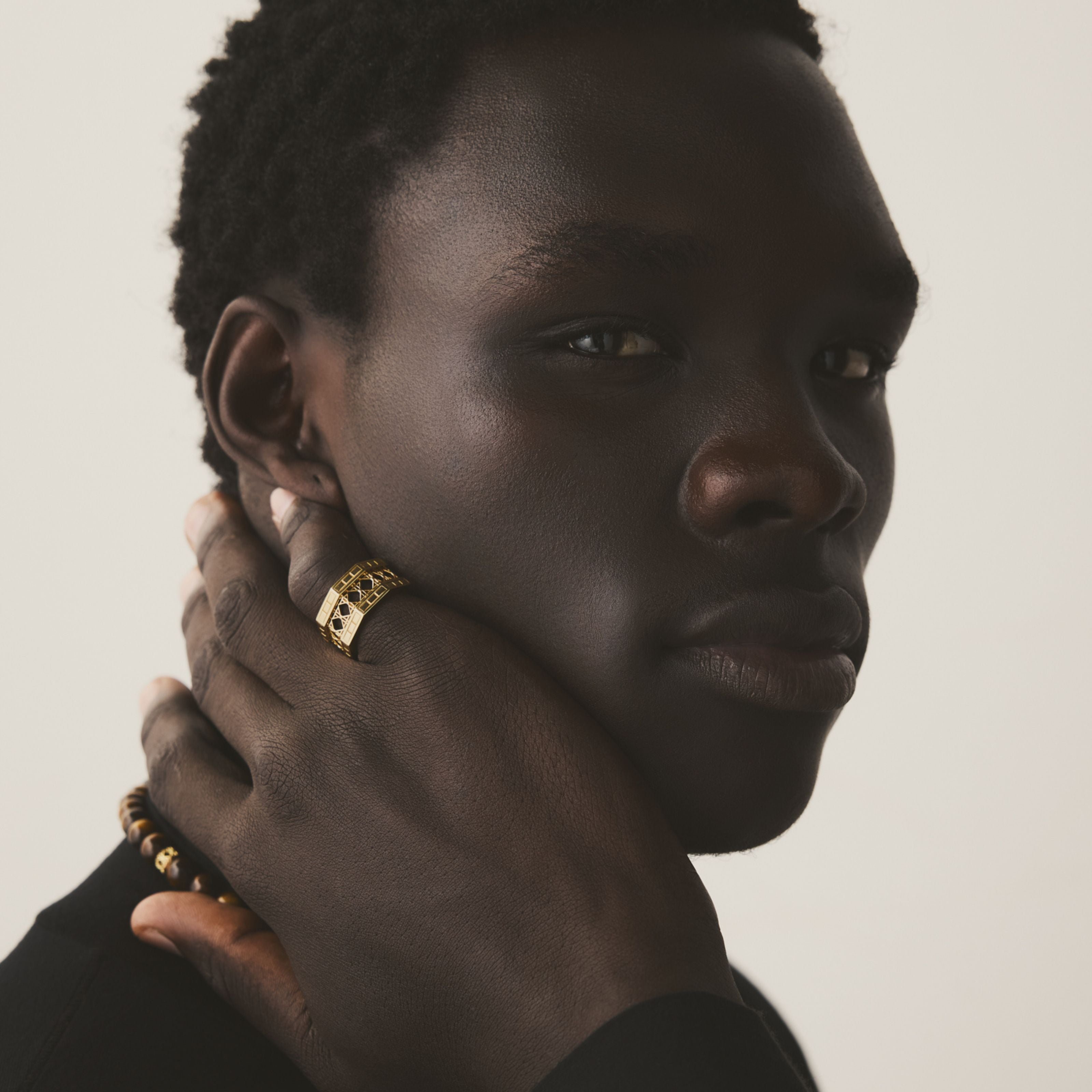 Male model wearing MoAnA LUU Doudou band ring in 18K yellow gold, featuring an intricate woven openwork design inspired by Caribbean fish traps.