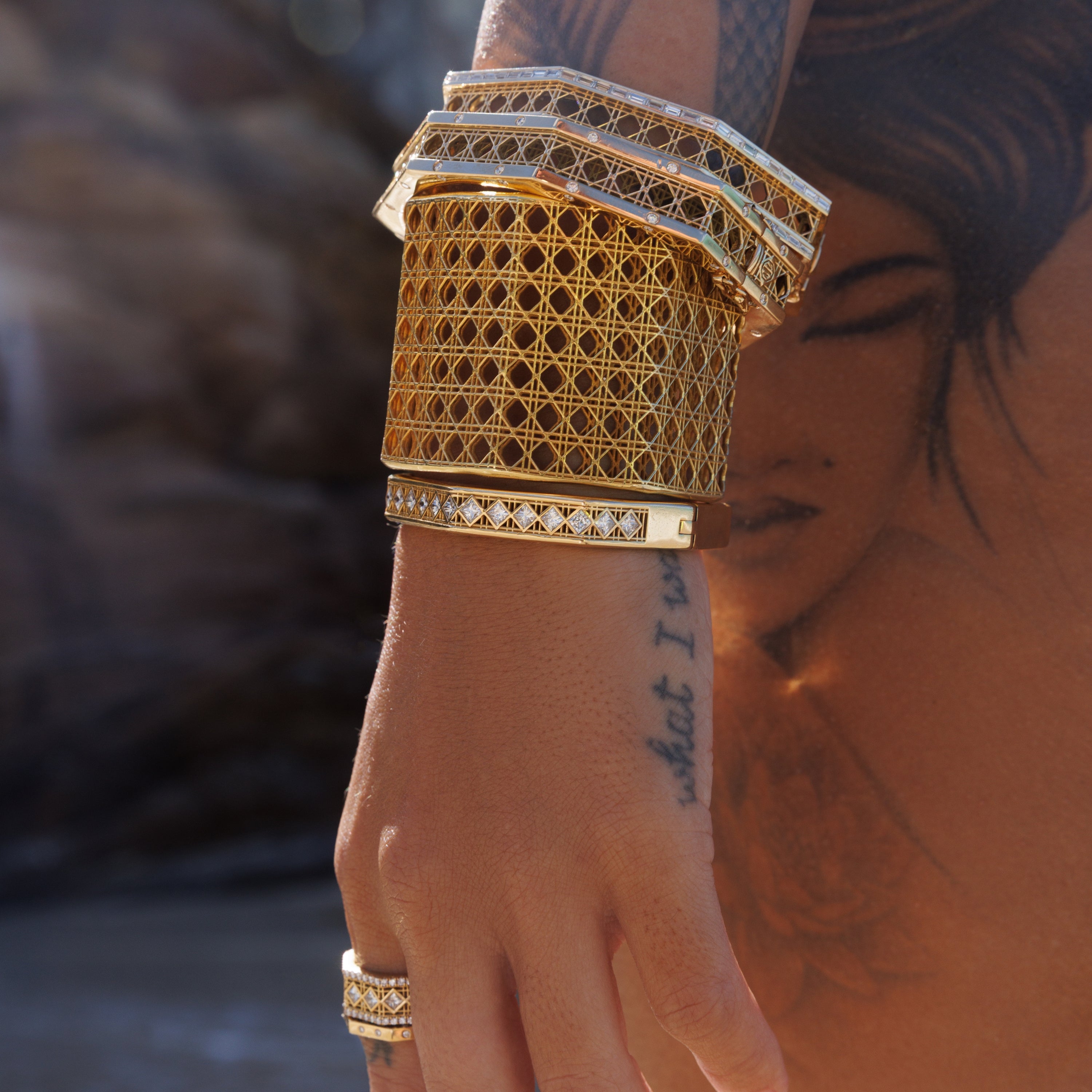 MoAnA LUU Doudou cuff bracelets in 18K yellow gold with diamond details, featuring intricate woven design inspired by Caribbean fish traps, worn stacked on model’s wrist.