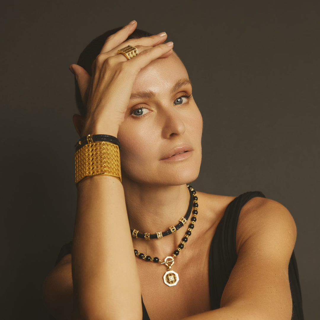 MoAnA LUU fine jewelry in 18K yellow gold worn layered on model, featuring onyx bead necklaces, pearl pendant, stingray leather bracelet and choker, and sculptural gold ring inspired by Creole design.