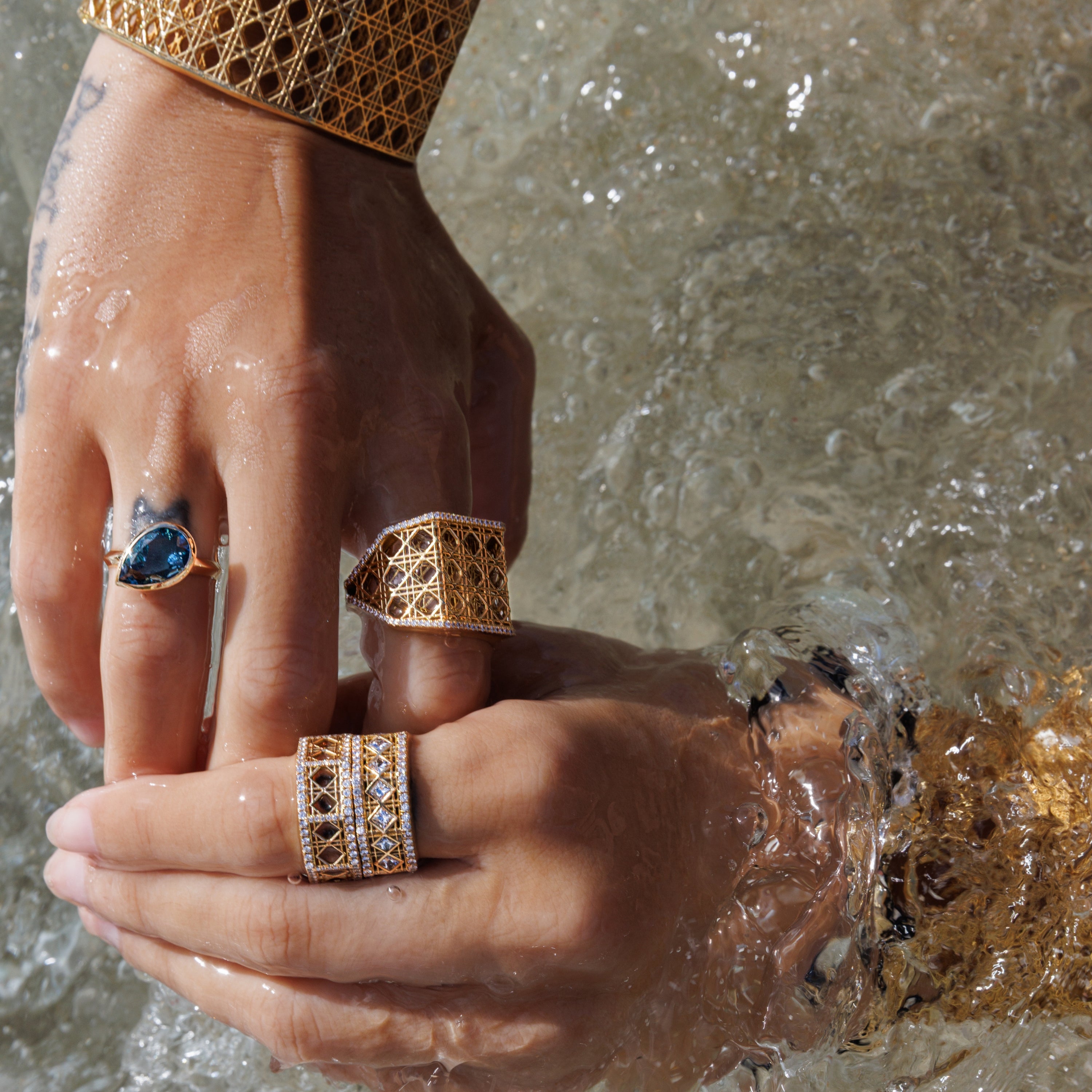 MoAnA LUU Doudou 18K gold rings with woven cane design and Dlo pear-shaped London blue topaz ring worn on model, showcasing sculptural Creole-inspired jewelry.