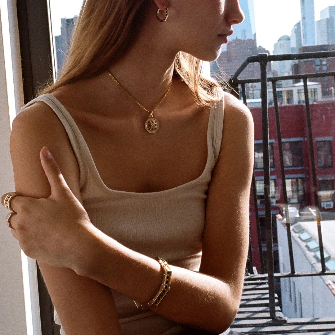 MoAnA LUU fine jewelry worn on model, featuring Ti hoops and diamonds, paired with Doudou octagonal pendant necklace, rings and bracelets in 18K yellow gold inspired by Caribbean fish traps.