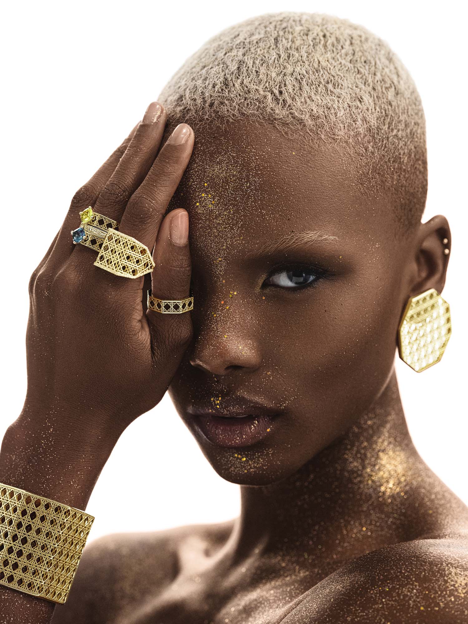 Model wearing MoAnA LUU Doudou statement octogonal earrings, cuff and rings in 18K yellow gold, featuring geometric woven openwork design inspired by Caribbean fish traps.